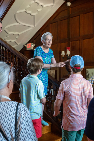 Historian Joan Leckie Salvas leads a museum tour at Rutherfurd Hall, engaging a multigenerational group of visitors at the base of the grand staircase inside the historic mansion.